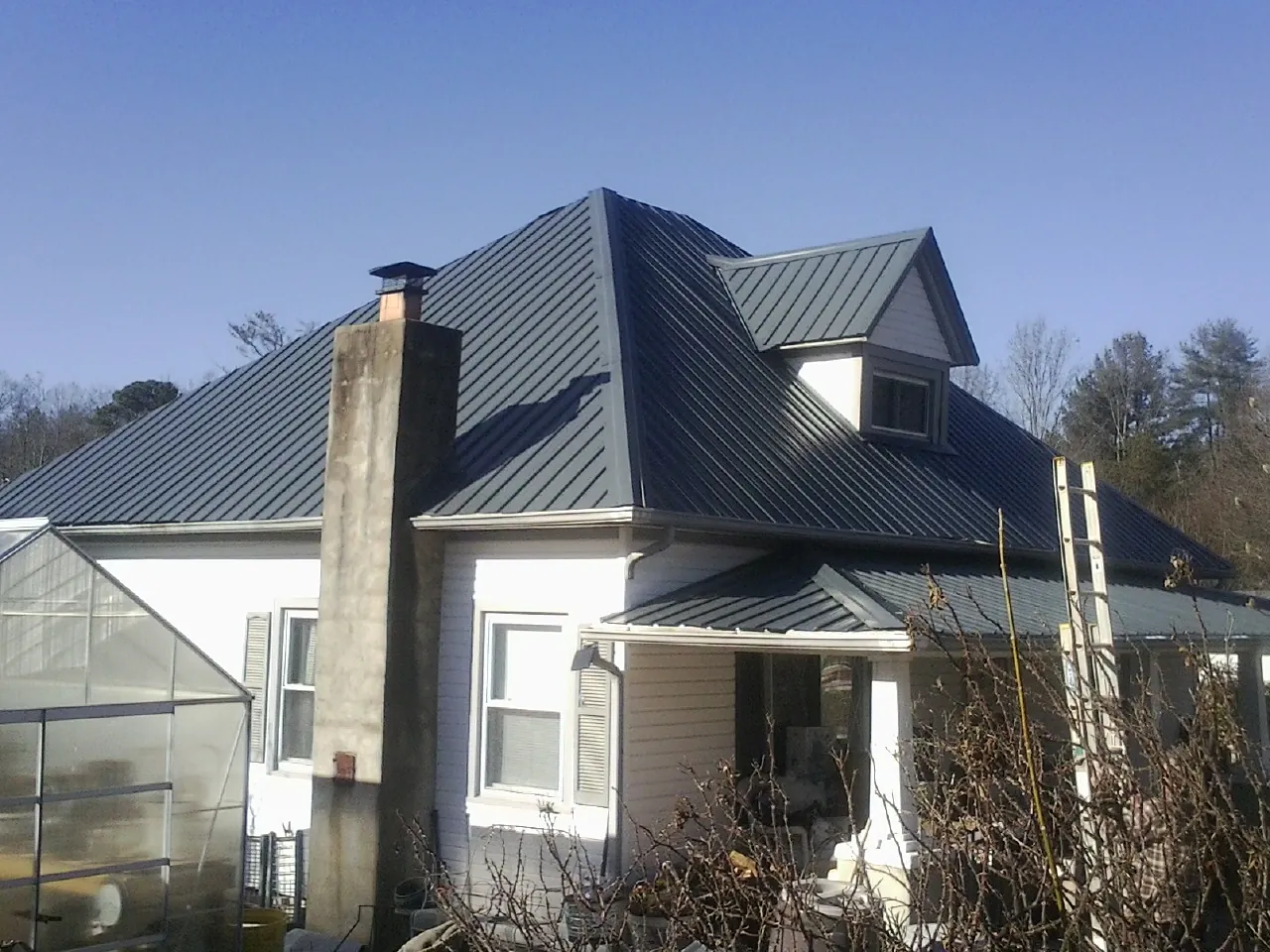 Dark blue standing seam metal roof on a white farmhouse with dormer — Slate & Tile Roof Repair by Roofing Brothers in Port Byron