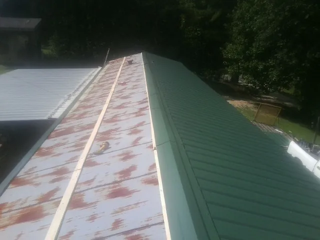 Old rusted panels beside newly installed green metal roofing — Wind Damage Roof Repair by Roofing Brothers in Port Byron