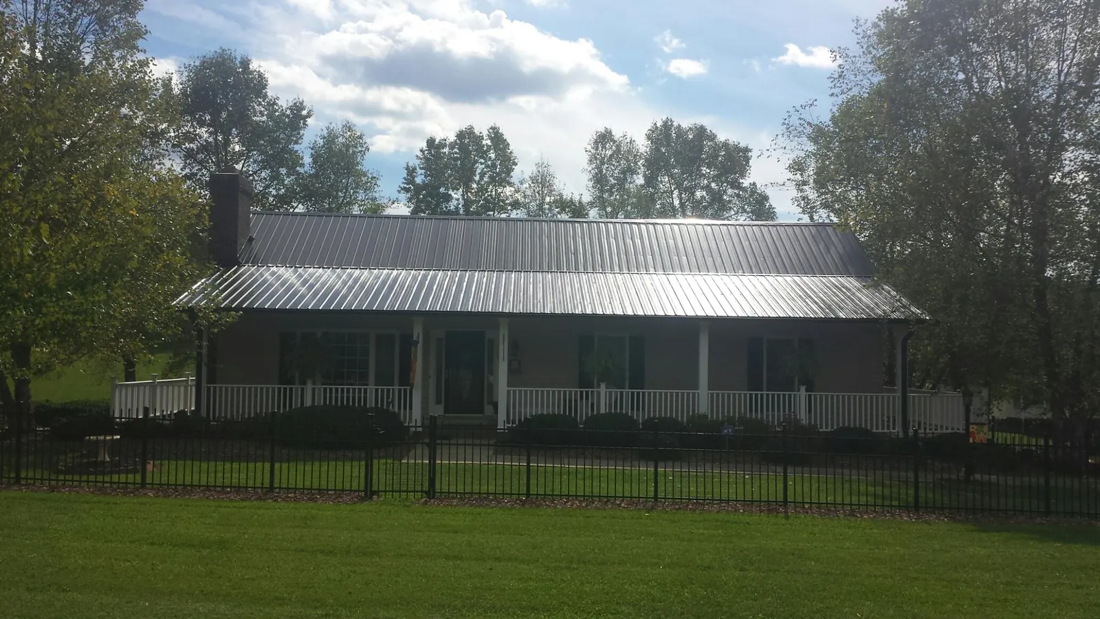 Gray metal roof on a brick ranch with a full width front porch — Gutter Guard Installation work by our crew in Port Byron